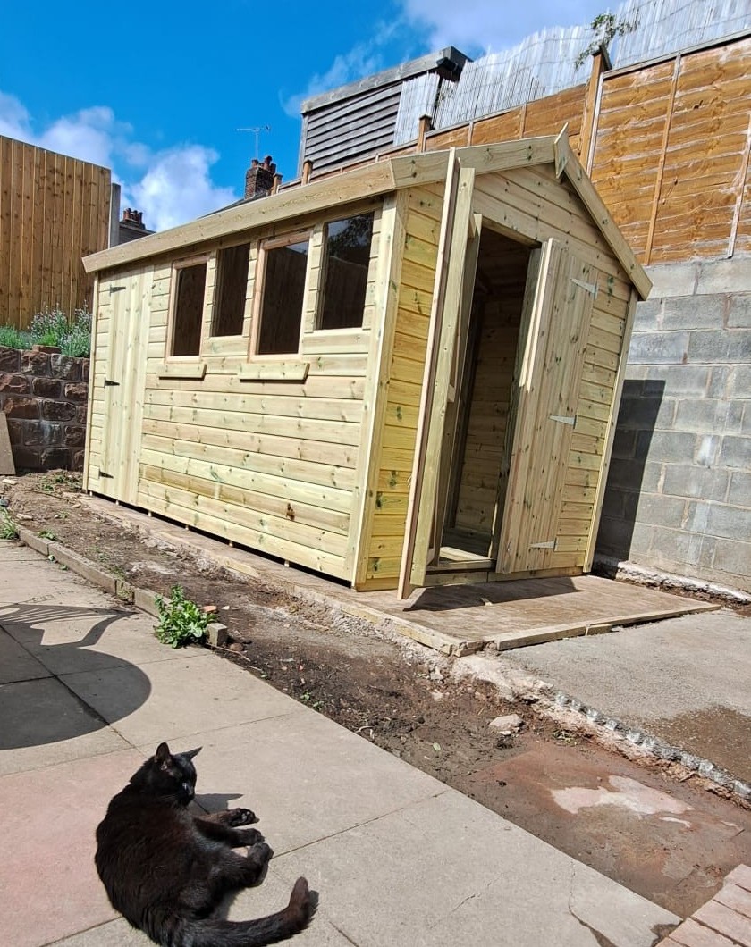 A new timber shed with four windows and open double doors in a back garden