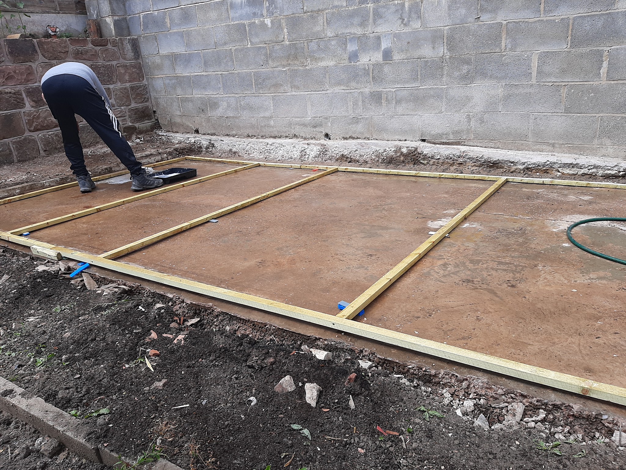 A timber base frame being laid out on a concrete pad against a block wall